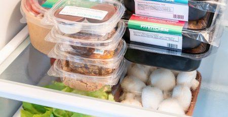 view of an open fridge filled with meal prep containers, fruits, and vegetables, indicating healthy eating habits.