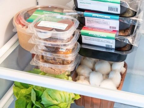 view of an open fridge filled with meal prep containers, fruits, and vegetables, indicating healthy eating habits.