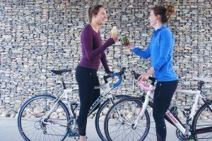 Two girls on bicycle having healthy drink in their hands