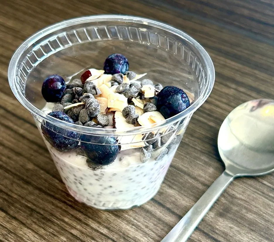 A glass of yogurt with blueberries and nuts and a spoon placed near it
