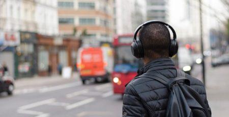 A person wearing headphones and a black jacket with a backpack standing on the sidewalk of a city