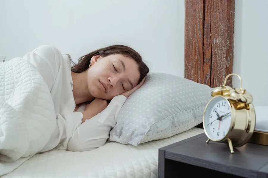 A woman peacefully sleeping in bed next to an alarm clock