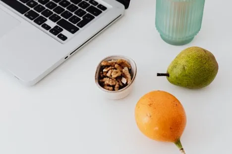 A laptop sits partially open on a white surface next to a small bowl of walnuts