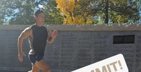 Man running outdoors with COMMIT text overlay, near a wall with inscriptions and trees with autumn leaves