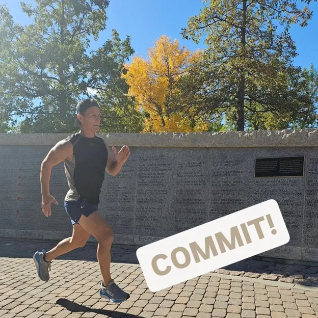 Man running outdoors with COMMIT text overlay, near a wall with inscriptions and trees with autumn leaves