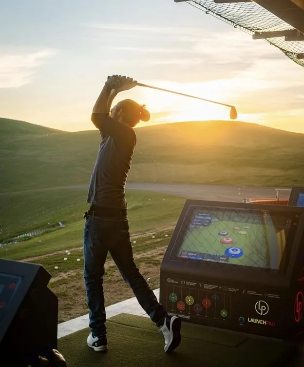 Person playing golf during sunset at a driving range with electronic score tracker