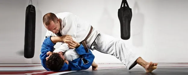 Two judo practitioners sparring in a dojo, one in a white gi, the other in blue