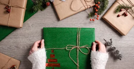 Hands holding a green Christmas gift among other wrapped presents on a wooden table