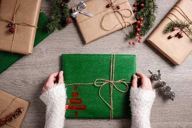 Hands holding a green Christmas gift among other wrapped presents on a wooden table