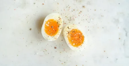 A halved boiled egg with a runny yolk sprinkled with pepper on a marble surface