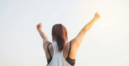 Person with arms raised in triumph against a clear sky