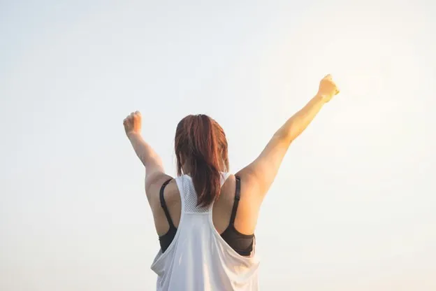 Person with arms raised in triumph against a clear sky