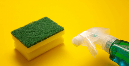 Green scrub pad with the top portion of a spray bottle on a yellow background